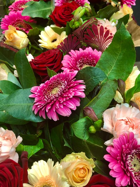 A vibrant floral arrangement featuring pink gerbera daisies with layered petals and yellow centers, complemented by red roses with tightly packed petals and soft peach and cream-colored eustoma flower